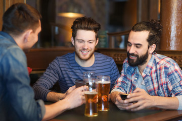 male friends with smartphones drinking beer at bar