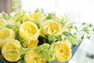 beautiful yellow English roses flower bouquet on wooden table next to window with sun light