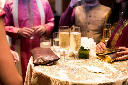 People dressed in rich Indian style stand around the table with