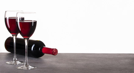 Zwei gefüllte Weingläser und eine Weinflasche auf Granttisch vor weißem Hintergrund. Makro, Panorama