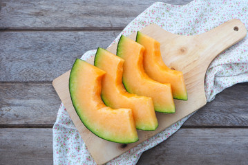 Top view of sliced rock melon on a wooden cutting board.