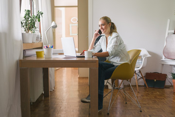 Always has a time for chatting with friends. Young student using her cellphone while sitting by her laptop