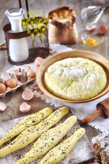 Bread sticks and yeast dough ready for baking, rustic setting on a wooden table.