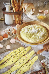 Bread sticks and yeast dough ready for baking, rustic setting on a wooden table.