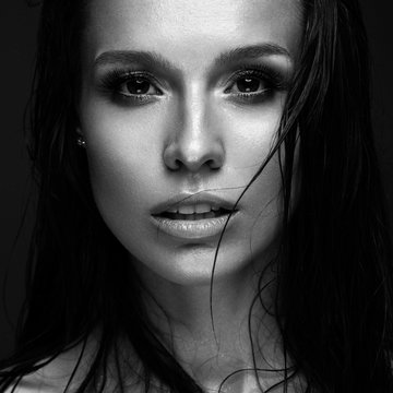 Beautiful girl with a bright make-up and wet hair and skin. Beauty face. Black and white photo. Picture taken in the studio on a black background.