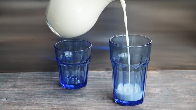 Pouring fresh milk into blue glasses. 