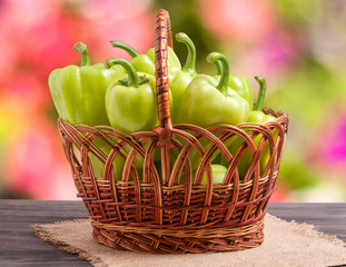 green bell peppers in a wicker basket on  wooden table with  blurred background