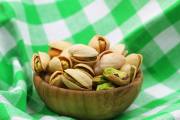 Pistachio nuts in wooden bowl on green and white checkered cloth with copy space
