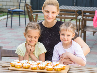 Mom and two daughters sitting at a table on which lay cooked them Easter cupcakes