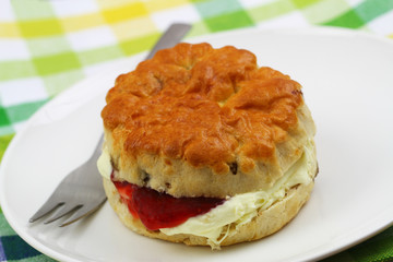 Freshly baked English scone with traditional clotted cream and strawberry jam on white plate, closeup
