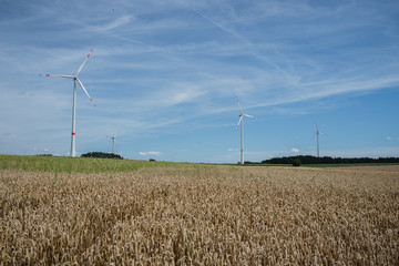 Landschaft mit Feldern und darunter Windkrafträder zur Stromgewinnung.