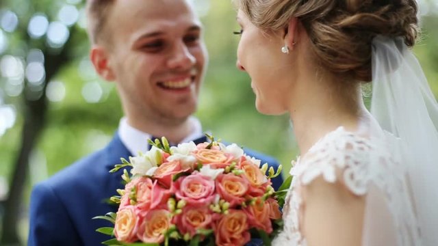 Happy smiling bride and groom on their wedding day posing with bridal bouquet outdoors