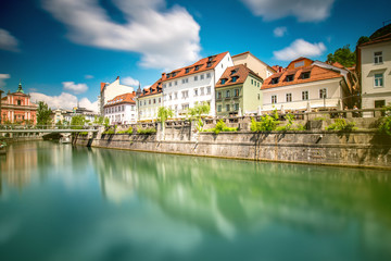 Fototapeta na wymiar View on Ljubljanica river with old building in Ljubljana city in Slovenia. Long exposure image technic with blurred clouds and reflection on the water