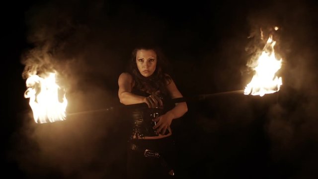 Female fire dance performer dancing with burning fire on black background. Brunette woman juggles with fireballs dance show outdoors