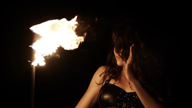 Close-up portrait of female fire dance performer dancing with burning fire on black background. Brunette woman juggles with fireballs dance show outdoors