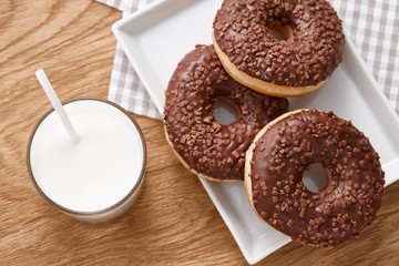 Glass of milk and chocolate donuts on wooden table