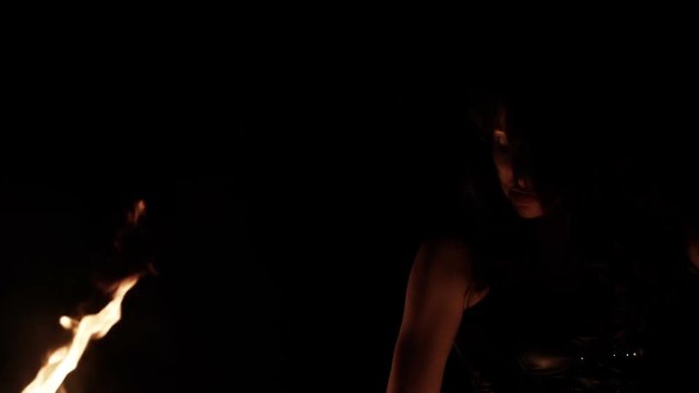 Close-up portrait of female fire dance performer dancing with burning fire on black background. Brunette woman juggles with fireballs dance show outdoors
