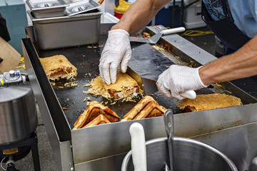 Man cooking grilled sandwiches at an outdoor carnival.