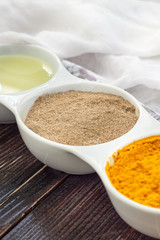 Turmeric, black pepper and olive oil in white ceramic bowl on wooden background. Ingredients for golden paste