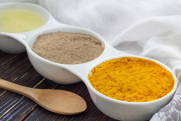 Turmeric, black pepper and olive oil in white ceramic bowl on wooden background. Ingredients for golden paste