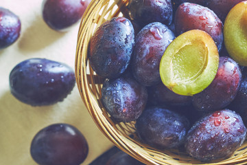 Fresh plums in weaved basket on wooden table. Top view