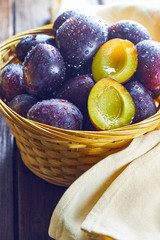 Fresh plums in weaved basket on wooden table