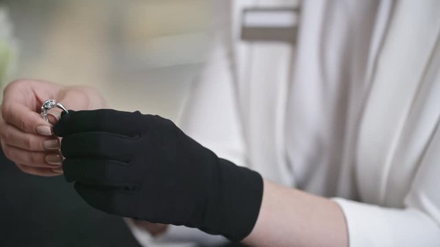 Closeup of female shop assistant hands in black glove holding and showing beautiful silver emerald ring