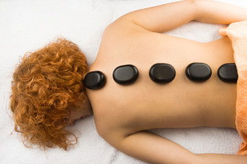 Beautiful woman with curly hair relaxing with hot stones on body on white towel