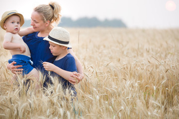 Portrait of happy family: young beautiful mother, adorable toddler boy and cute kid walking in the wheat field and enjoying sunny day. Mom with children. Lifestyle concept