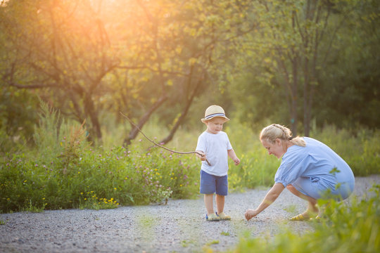 Cute little toddler boy watching his mother drawing on the raod. Mom and son on sunset walk in the park. Lifestyle and motherhood concept
