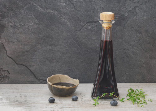 Blueberry vinegar in glass bottle with fresh blueberries and thyme on rustic table. 