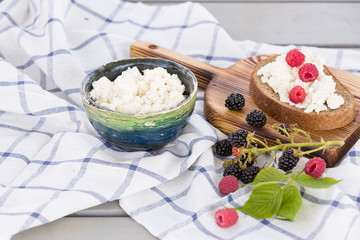 Organic Farming Cottage cheese in a green bowl, slice of whole wheat bread with Homemade Ricotta cheese served with raspberries and blackberries on wooden board  on linen fabric