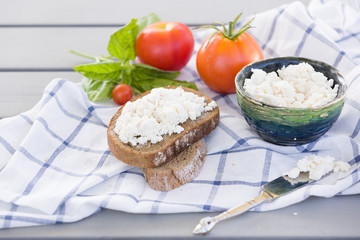 Organic Farming Cottage cheese in a green bowl, slice of whole wheat bread with Homemade Ricotta cheese served with tomatoes and basil on wooden board  on linen fabric. Healthy food concept
