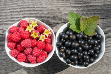 Raspberries and black currants in two cups on wooden surface the view from the top