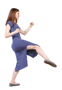 skinny woman funny fights waving his arms and legs. Isolated over white background. The brunette in a blue striped dress in a fighting stance.