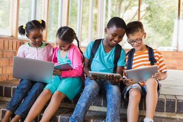 Kids sitting on staircase using laptop and digital tablet