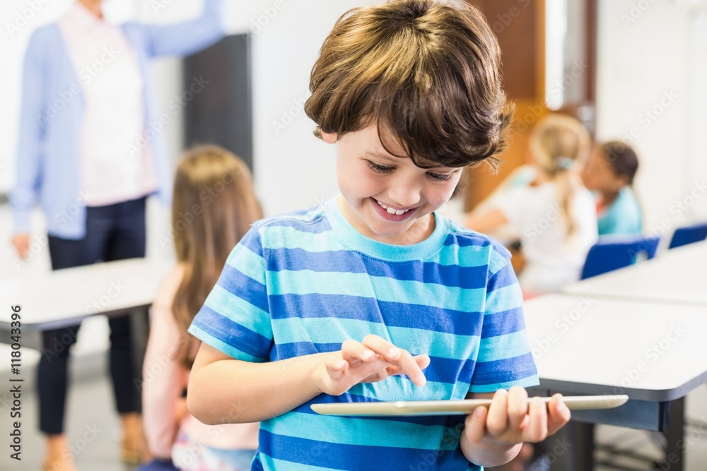 Poster Smiling schoolboy using digital tablet in classroom