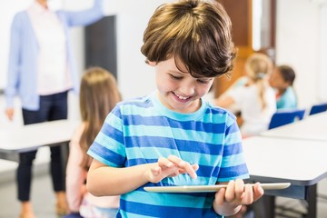 Smiling schoolboy using digital tablet in classroom