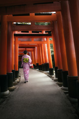 Woman dressed in traditional japanese costume walking under tori gates at the fushimi-inari shrine,...