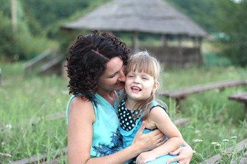 cheerful mother plays with little daughter in meadow in summer