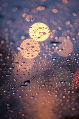 Rain drops on window with road light bokeh, rainy season abstract background,water drop on the glass, night storm raining car driving concept.