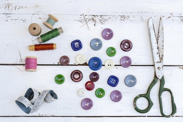 Set of several pied buttons for garment with threads, garment tape and scissors on a bright wooden background