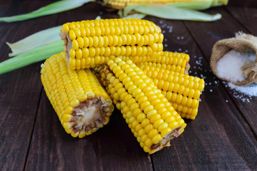 Cooked and raw corncobs on a dark wooden background.