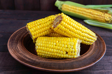 Cooked and raw corncobs on a dark wooden background.