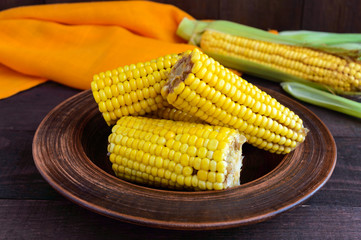 Cooked and raw corncobs on a dark wooden background.