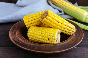 Cooked and raw corncobs on a dark wooden background.
