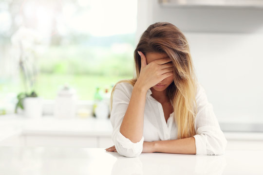 Young sad woman suffering from headache in kitchen