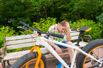 Young man with sad expression sitting on bench near bike