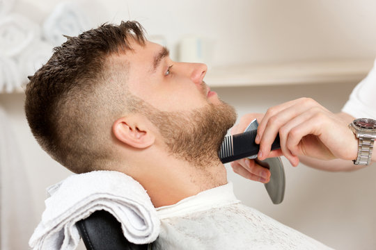 Young bearded man getting beard haircut by hairdresser at barber