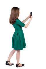 back view of standing young beautiful  woman  using a mobile phone. girl  watching. Rear view people collection.  backside view of person.  Isolated over white background. The slender brunette in a